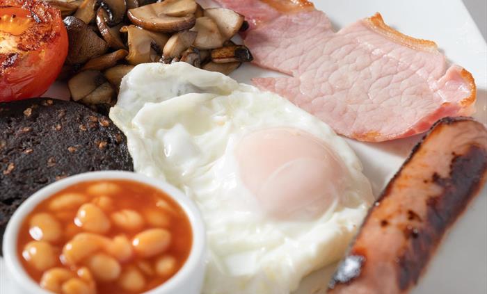 A hearty homemade full Welsh breakfast, featuring locally sourced ingredients. Savoury Welsh back bacon, succulent sausages, egg​ cooked to perfection